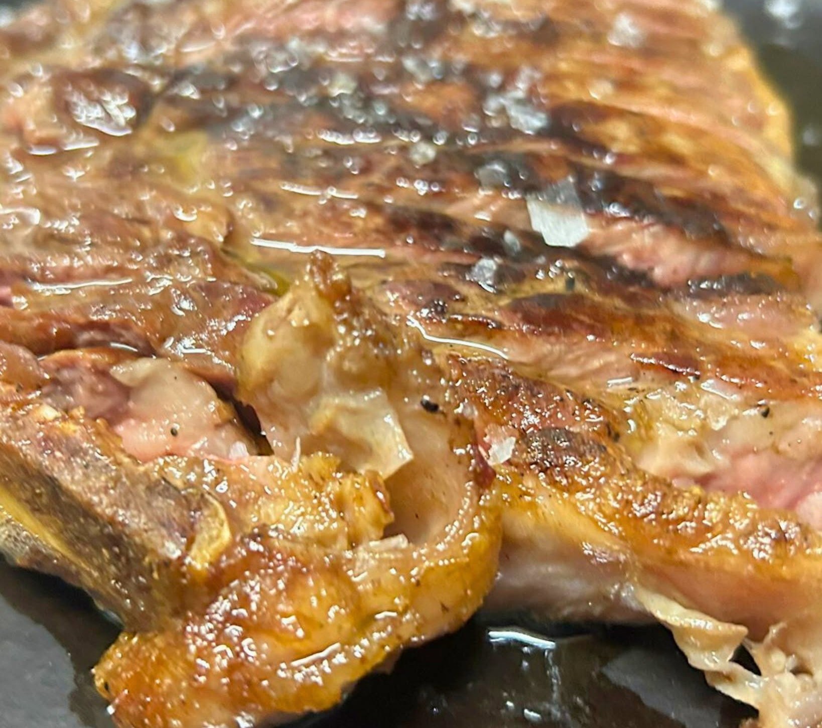 Bistecca alla griglia di Ai Navigli in primo piano, crosta dorata, sale grosso e olio su un piatto scuro